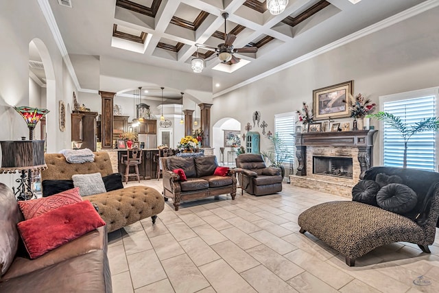 living room featuring arched walkways, ceiling fan, a stone fireplace, a towering ceiling, and ornate columns