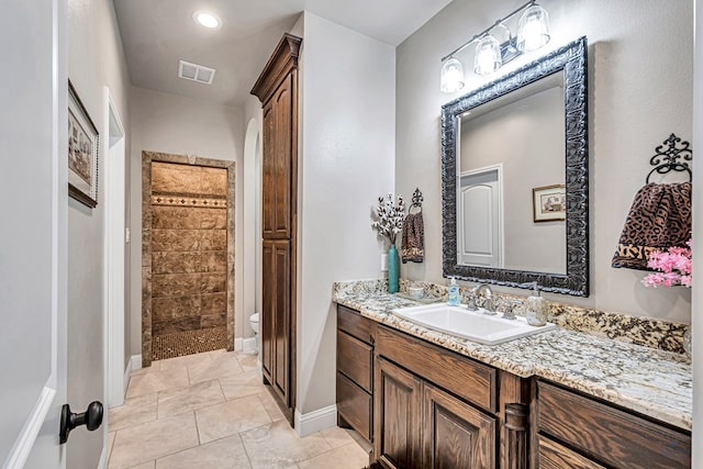 bathroom with visible vents, toilet, a tile shower, vanity, and baseboards