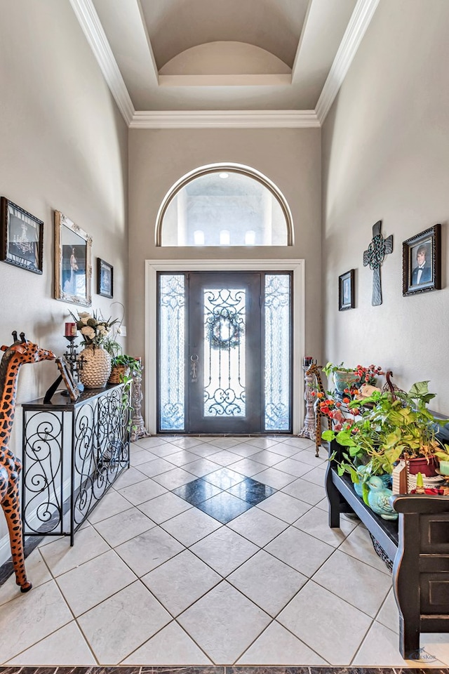 entrance foyer with light tile patterned floors, a high ceiling, ornamental molding, and a raised ceiling
