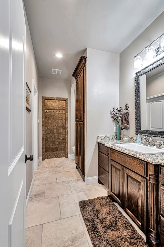 full bath featuring toilet, vanity, visible vents, baseboards, and a tile shower