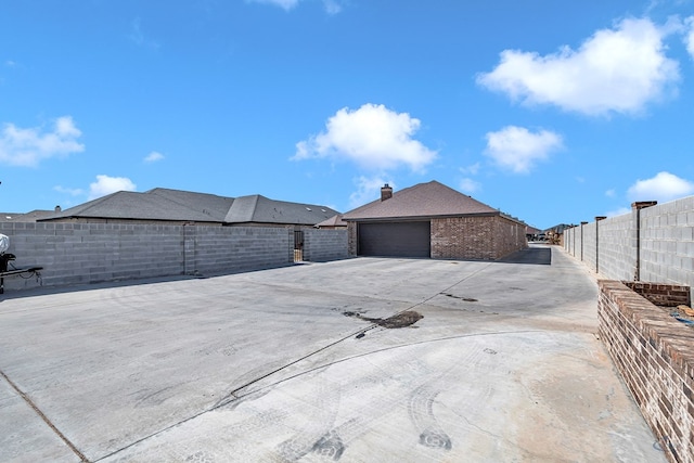 exterior space featuring a fenced backyard, a chimney, a detached garage, and brick siding