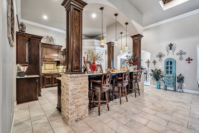 kitchen with pendant lighting, dark brown cabinetry, a breakfast bar, decorative columns, and crown molding