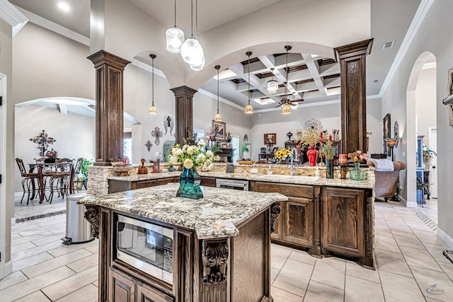 kitchen featuring decorative columns, visible vents, coffered ceiling, a kitchen island, and stainless steel microwave