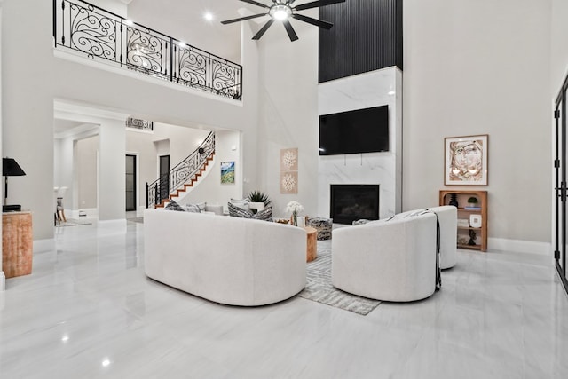 living room featuring ceiling fan, a fireplace, and a towering ceiling