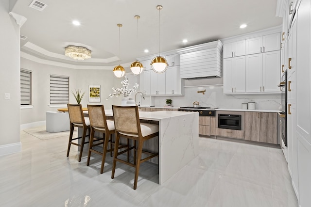 kitchen with white cabinets, pendant lighting, light stone counters, and a kitchen island with sink