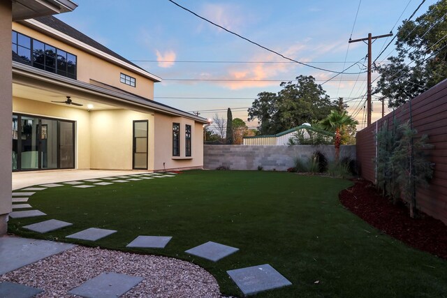 yard at dusk featuring ceiling fan