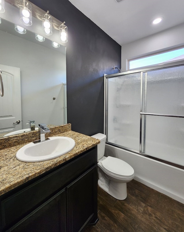 bathroom with vanity, toilet, wood finished floors, and shower / bath combination with glass door