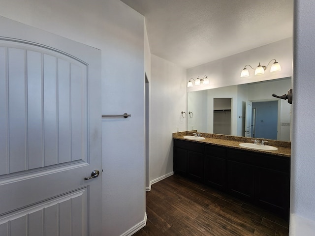 full bathroom featuring a sink, baseboards, wood finished floors, and double vanity