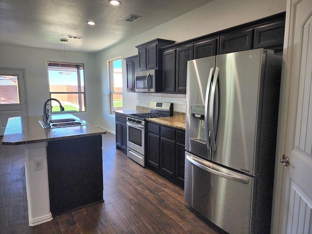 kitchen with dark wood finished floors, a sink, stainless steel appliances, dark cabinets, and backsplash