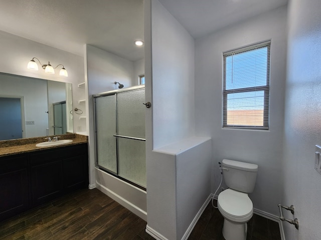 bathroom with baseboards, bath / shower combo with glass door, toilet, wood finished floors, and vanity