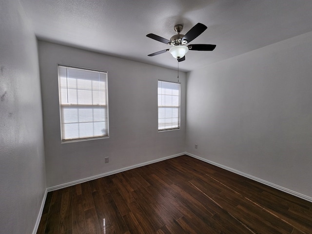 unfurnished room featuring dark wood-type flooring, a ceiling fan, and baseboards