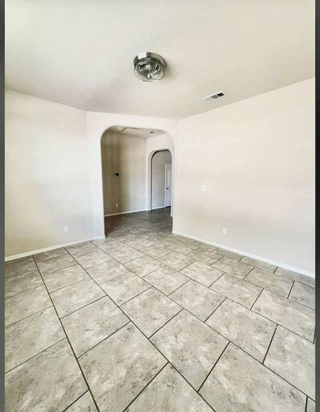spare room featuring arched walkways, baseboards, and light tile patterned flooring