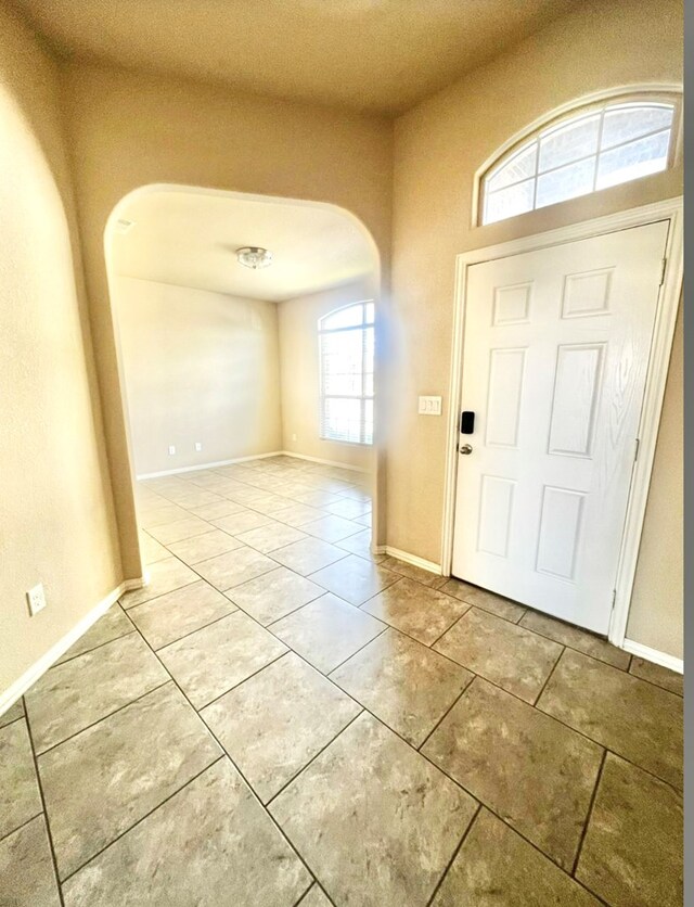 foyer featuring arched walkways, light tile patterned floors, and baseboards