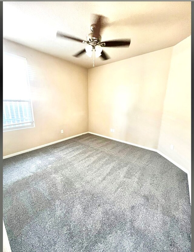 spare room featuring ceiling fan, dark carpet, and baseboards