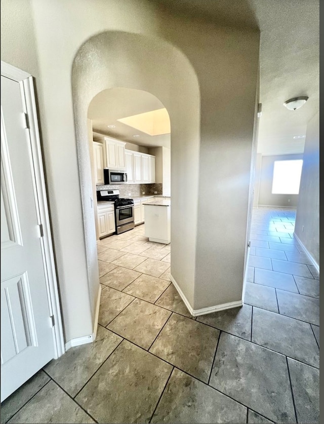 hall featuring baseboards, light tile patterned floors, and arched walkways