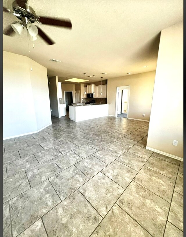 unfurnished living room featuring a ceiling fan and baseboards
