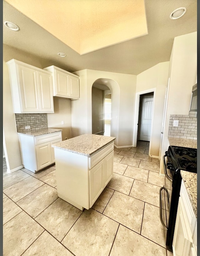 kitchen featuring black range with gas stovetop, arched walkways, backsplash, a raised ceiling, and recessed lighting