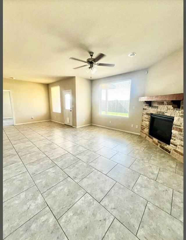 unfurnished living room with light tile patterned flooring, baseboards, a stone fireplace, a ceiling fan, and a textured ceiling