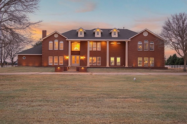 back of property at dusk with french doors, a lawn, and brick siding