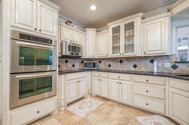 kitchen featuring stainless steel appliances, cream cabinetry, backsplash, and glass insert cabinets