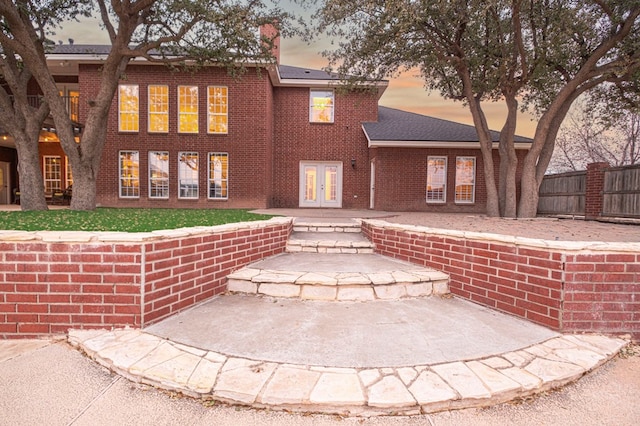 view of front of home with french doors, brick siding, fence, and a patio