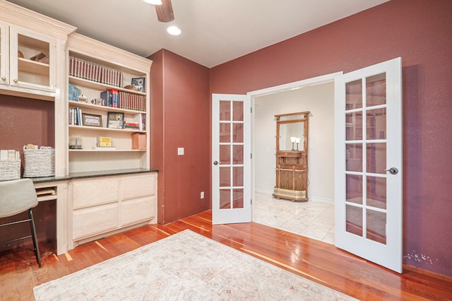 unfurnished office featuring built in study area, a ceiling fan, wood finished floors, and french doors