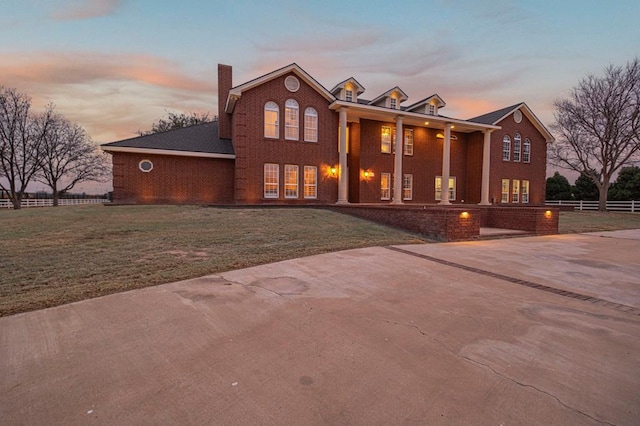 view of front facade with a lawn, concrete driveway, a chimney, fence, and brick siding