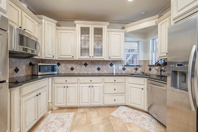 kitchen with stainless steel appliances, cream cabinetry, backsplash, and a sink