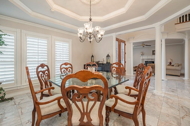 dining space featuring ceiling fan with notable chandelier, a tray ceiling, a fireplace, and ornate columns