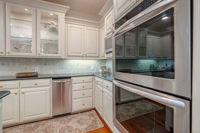 kitchen with light wood-type flooring, stainless steel double oven, backsplash, and dark countertops