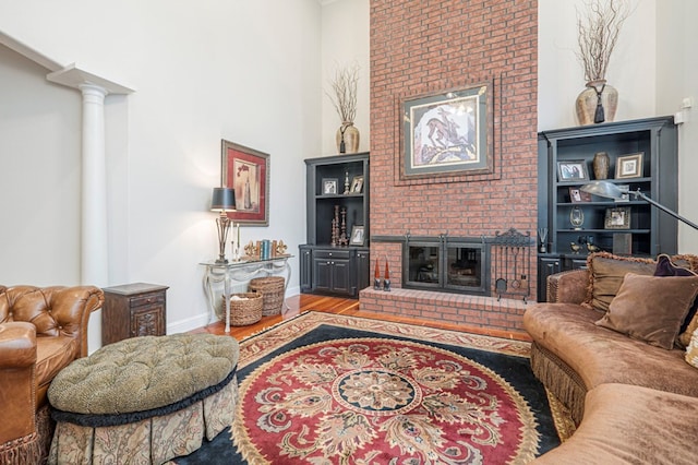 living area with decorative columns, baseboards, a towering ceiling, wood finished floors, and a fireplace