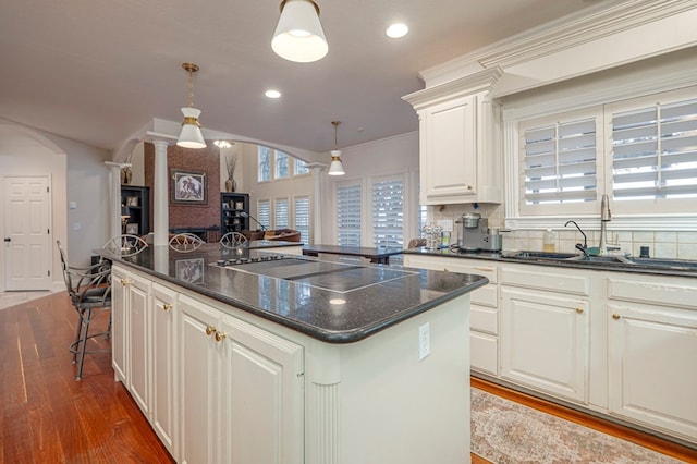 kitchen featuring arched walkways, a kitchen island, a sink, dark wood finished floors, and decorative columns