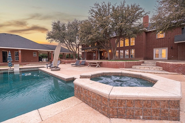 pool at dusk featuring an outdoor pool, french doors, a patio, and an in ground hot tub