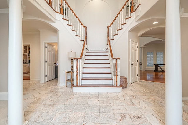 foyer entrance with crown molding, marble finish floor, a high ceiling, and baseboards