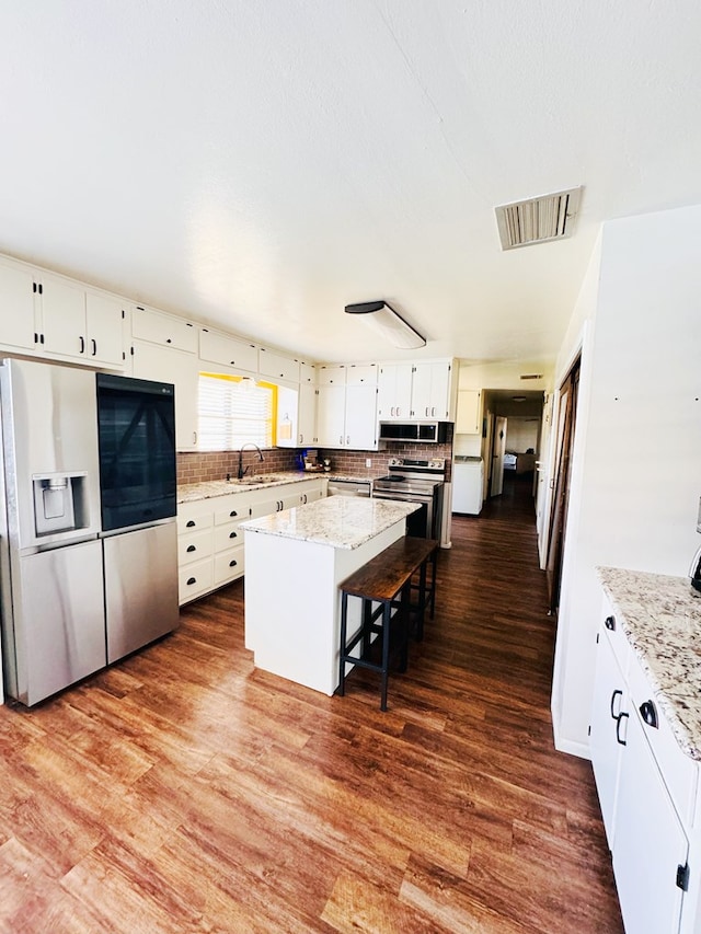 kitchen featuring dark wood-type flooring, a breakfast bar area, a kitchen island, white cabinetry, and stainless steel appliances