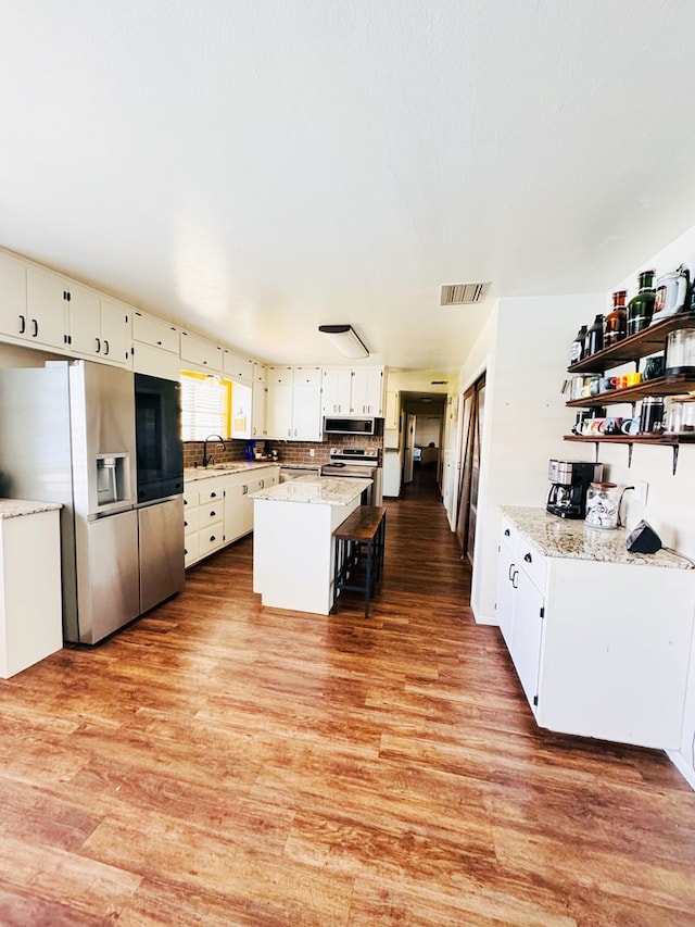 kitchen featuring a center island, white cabinets, light hardwood / wood-style flooring, light stone countertops, and stainless steel appliances