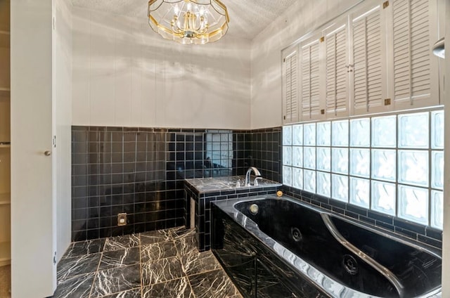 bathroom with a textured ceiling, a tub to relax in, and a chandelier