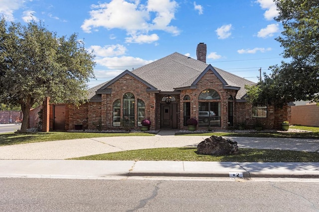 tudor house featuring a front yard, a chimney, brick siding, and a shingled roof