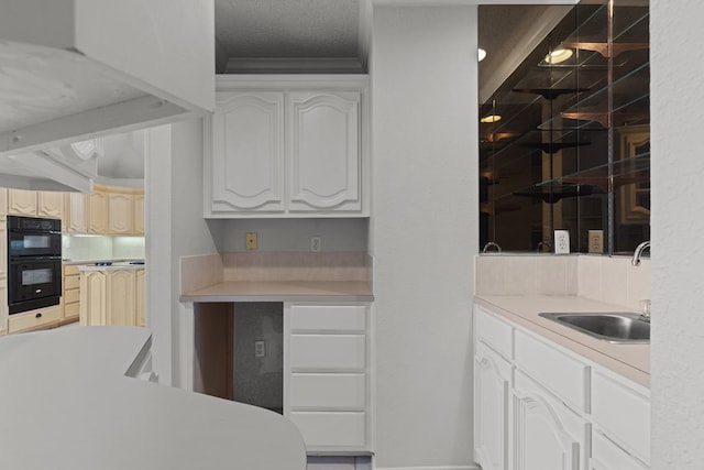 kitchen featuring light countertops, dobule oven black, white cabinets, and a sink