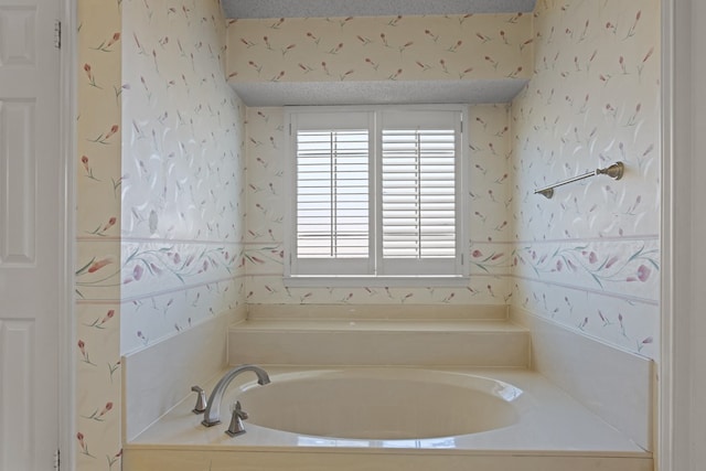 bathroom featuring a bath, a textured ceiling, and wallpapered walls