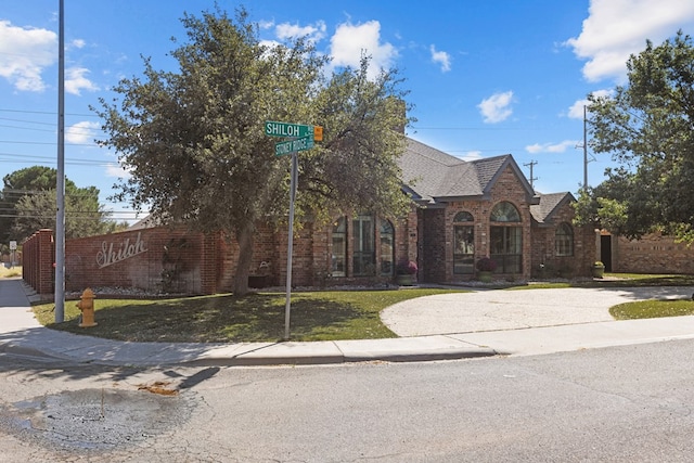 english style home featuring brick siding, a front lawn, and a shingled roof