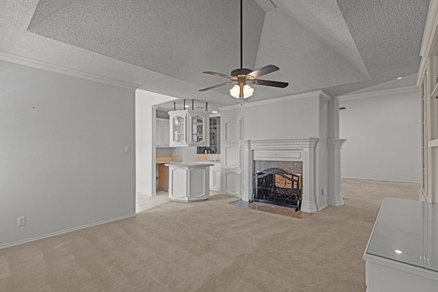 unfurnished living room with ceiling fan, a textured ceiling, a tiled fireplace, crown molding, and light colored carpet