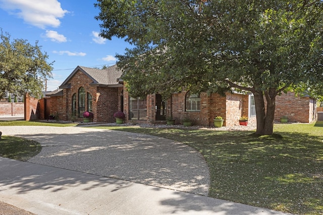 obstructed view of property featuring brick siding, curved driveway, and a front yard