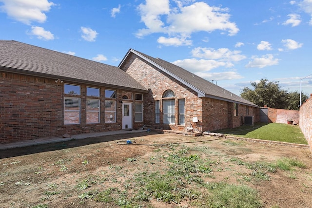 rear view of house with brick siding, central AC, a lawn, and fence