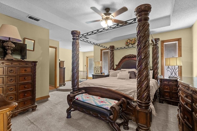 bedroom with ceiling fan, light colored carpet, a tray ceiling, and a textured ceiling