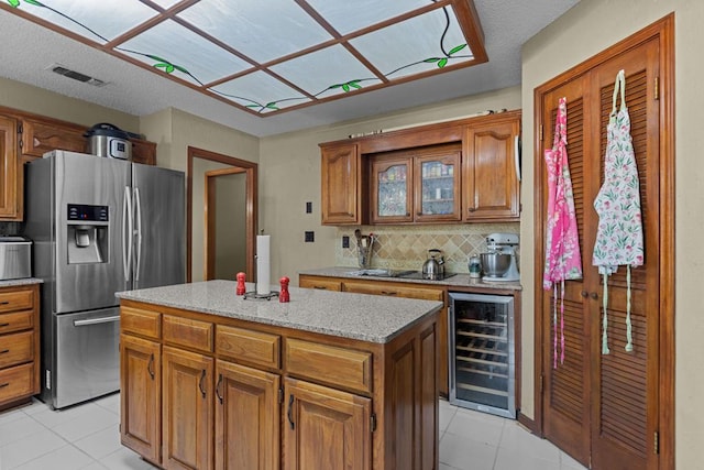 kitchen featuring beverage cooler, backsplash, a center island, light tile patterned floors, and stainless steel refrigerator with ice dispenser