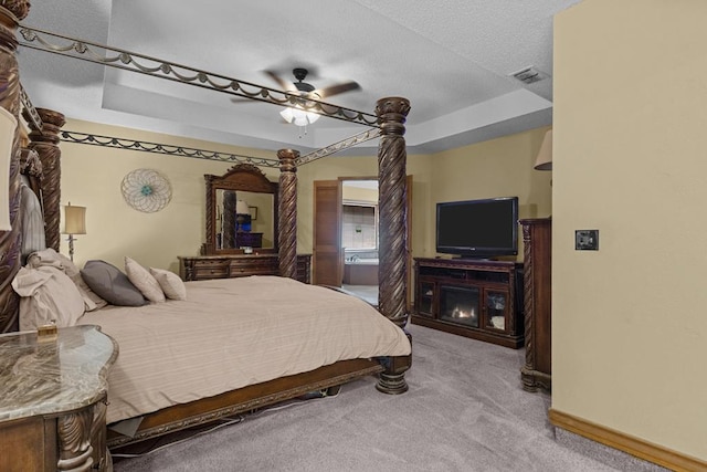 carpeted bedroom with ceiling fan, a tray ceiling, and a textured ceiling