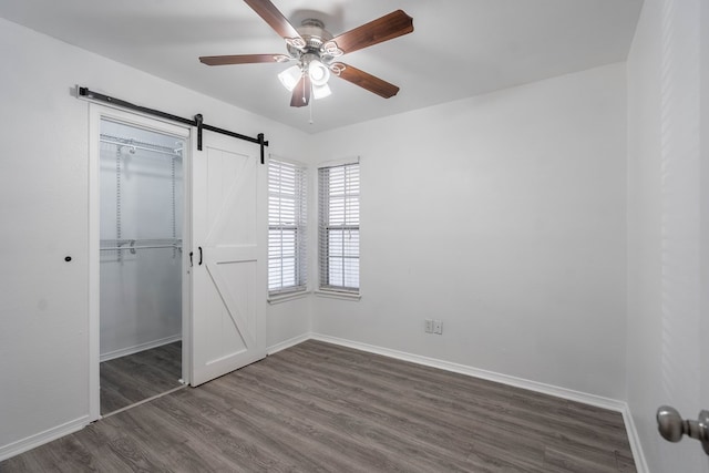 unfurnished bedroom featuring a barn door, baseboards, dark wood-style flooring, and a closet