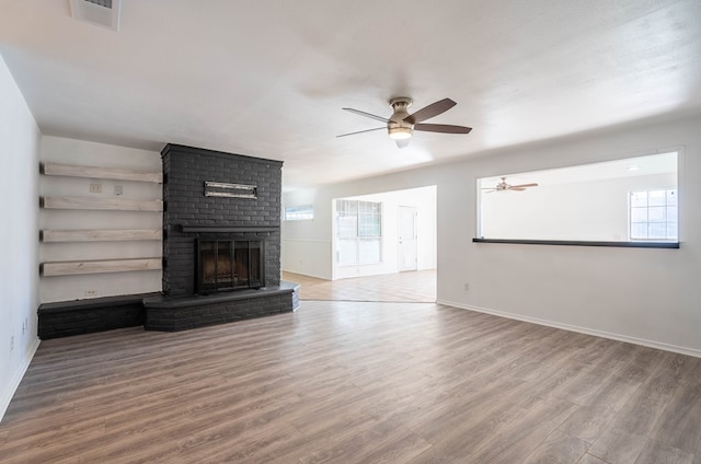 unfurnished living room featuring a brick fireplace, wood finished floors, visible vents, and baseboards