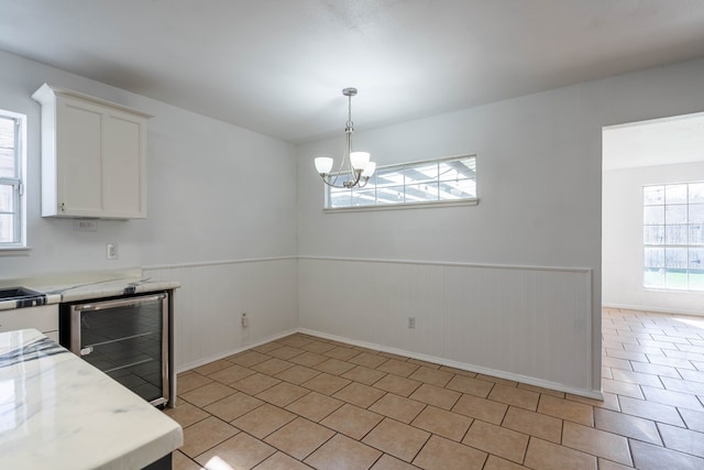 unfurnished dining area featuring beverage cooler, a chandelier, wainscoting, light tile patterned flooring, and a sink